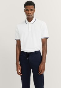 White polo shirt with navy-blue striped accents at the collar and sleeves, paired with dark navy pants. Simple, classic design.