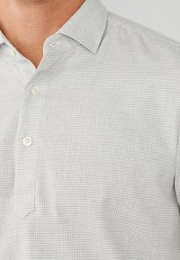 Een button-up shirt van lichtgrijs materiaal met een gemêleerd ruitpatroon, voorzien van een smalle kraag en een verborgen knoopsluiting.