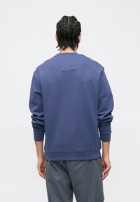 Sweatshirt azul marinho com gola redonda, punhos e barra canelados. Apresenta uma pequena etiqueta acima da gola traseira e textura suave.