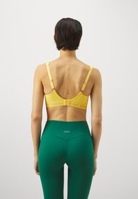 Gul sports-BH med mesh-detaljer, justerbare stropper, og rosa detaljer. Kombinert med høyt liv, grønne leggings med logo.