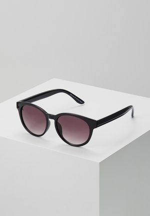 Schwarze Cat-Eye-Sonnenbrillen mit einem verlaufenden rosafarbenen Gläsern. Sie verfügen über dicke Rahmen und gerade Bügel und ruhen auf einer flachen, weißen Oberfläche.