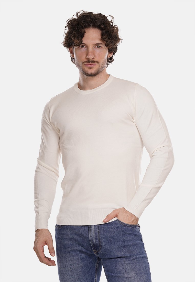 Maglione a maniche lunghe di colore crema chiaro, in un design aderente. Collo e polsini a coste con una texture liscia. Indossato con jeans blu.