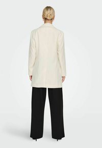 Blazer blanc au design structuré, manches longues et fente arrière simple, associé à un pantalon noir à jambes larges. Textured de tissu lisse.