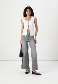 Witte geribbelde mouwloze top met golvende randen, grijze wijde jeans en zwarte ballerina's. Geassorteerd met een kleine zwarte handtas.