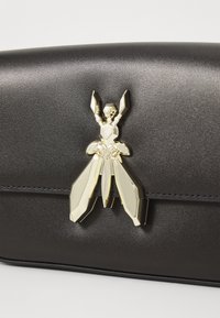Borsa sintetica nera con finitura lucida, dotata di una chiusura a forma di insetto in metallo con accenti dorati e argentati. Design minimalista, forma rettangolare.