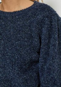 Navyblaues, strukturiertes Sweatshirt mit Rundhalsausschnitt, aus einem flauschigen Strickmaterial mit weicher Oberfläche. Es zeigt einen Teil des Ärmels und des Kragens.