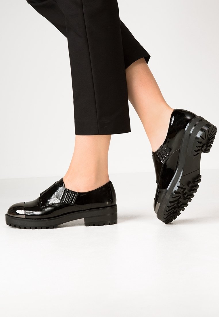 Chaussures en cuir verni noir avec une semelle épaisse, un bout carré et un panneau latéral élastique pour un enfilage facile. Semelle texturée pour une meilleure adhérence.