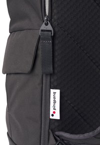 Schwarzer Stoff-Rucksack mit strukturierten Oberflächen, einem Reißverschluss, einem verstellbaren Tragegurt und einem kleinen weißen Markenschild mit drei farbigen Punkten.
