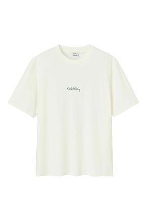 T-shirt en coton de couleur crème avec un col rond et des manches courtes, ornée d'un logo « Keith Haring » brodé en vert sur la poitrine.