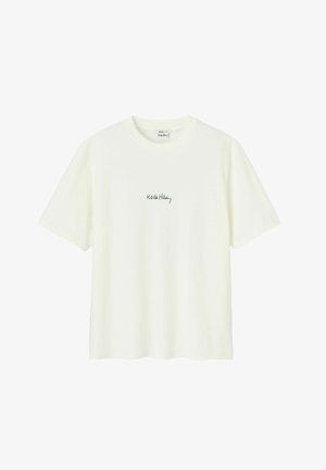 T-shirt en coton de couleur crème avec un col rond et des manches courtes, ornée d'un logo « Keith Haring » brodé en vert sur la poitrine.