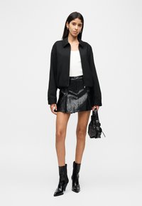 Μαύρο cropped bomber μπουφάν, λευκό εφαρμοστό τοπ, μαύρη δερμάτινη μίνι φούστα με πιέτες. Μαύρες ankle μποτάκια και μια μικρή τσάντα ολοκληρώνουν το σύνολο.