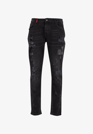 Vaqueros de mezclilla negra con detalles desgastados, que incluyen parches deshilachados, salpicaduras de pintura, un diseño clásico de cinco bolsillos y un acento rojo en la cintura.