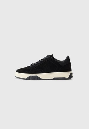 Black suede low-top sneaker with black laces, cream rubber sole, embossed logo on the side, and textured heel panel.
