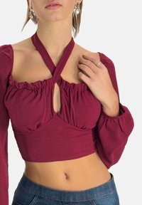 Bordeaux cropped top med puffede lange ærmer, der har en crossover halterneck og nøglehul detalje, lavet af et blødt, struktureret stof.