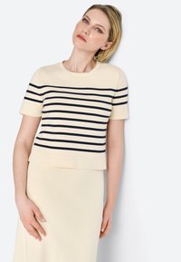 Haut en tricot crème avec des rayures horizontales bleu marine, manches courtes et un col rond ; associé à une jupe crème assortie. Texture lisse.