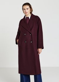 Cappotto doppiopetto in lana color bordeaux con grandi bottoni neri, rever a punta e due tasche laterali, caratterizzato da una vestibilità comoda e un tessuto leggermente strutturato.