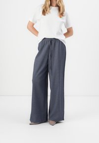 Pantalon à jambes larges en tissu gris foncé à finition texturée, doté d'une taille élastique et d'un cordon de serrage. Associé à un t-shirt blanc.