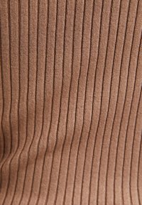 Ribbvävd trikå i en varm brun nyans, med vertikala ränder och en mjuk textur. Materialet verkar vara elastiskt och slätt.