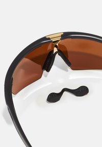 Schwarze Sonnenbrille mit braunen Gläsern, die an der Brücke einen goldenen Akzent und strukturierte schwarze Nasenpads für mehr Komfort aufweist. Der bronzene Farbton verbessert die Sicht.