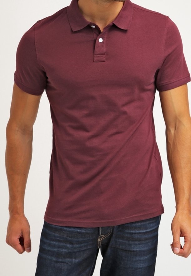 Homme portant un polo bordeaux ajusté à manches courtes et un jean bleu foncé, debout avec les bras détendus le long du corps.