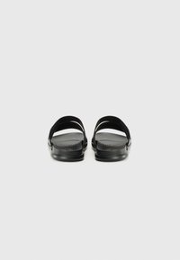 Black slide sandals with two wide straps, cushioned footbed, textured sole, and a smooth finish. Minimalist design and flat shape.