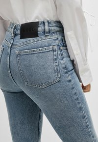 Ljusblå denimjeans med en figurnära passform, försedda med en svart läderetikett med "HUGO" vid midjan och två bakfickor.