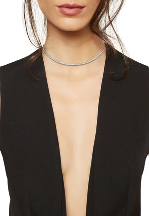 Collana choker in argento con un design liscio e piatto e una sottile texture. Indossata al collo, abbinata a un abbigliamento con scollatura a V profonda.