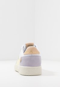 Białe sneakersy z żółtymi i lawendowymi akcentami, zamszowym obcasem, teksturowaną gumową podeszwą i złotym detalem logo z tyłu.