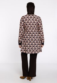 Kleurrijke gebloemde tuniek met bruine, crème en marineblauwe bladvormen; gladde stof; gecombineerd met donkerbruine pantalons en enkellaarsjes.