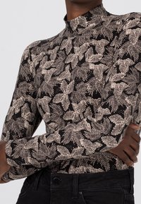 Långärmad polotröja i svart med ett krämfärgat blommönster. Har en figurnära silhuett och ett mjukt, texturerat tyg.