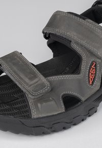 Gray sport sandal with adjustable Velcro straps, textured rubber sole, and mesh accents. Features a marked logo in red on the side.