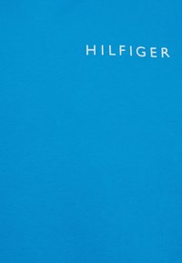 Camiseta de algodón azul con una textura suave y un logotipo blanco "HILFIGER" exhibido de manera prominente en el pecho.