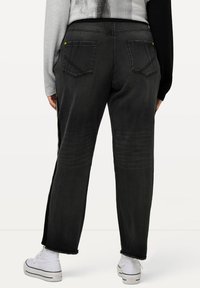 Vaqueros de mezclilla negra con un corte relajado, que cuentan con dos bolsillos traseros, costuras visibles y dobladillo sin terminar. Se combinan con zapatillas blancas de caña alta.