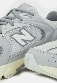 Gros plan sur des chaussures de sport New Balance grises et blanches avec tissu mesh, lacets et le grand logo N sur le côté.