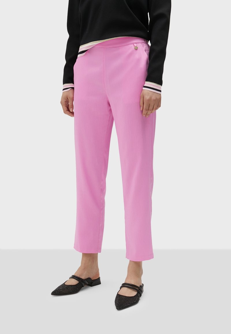 Rosa byxor med raka ben och texturerad yta, med sidoficka och en diskret logotypdetalj. Matchas med svarta spetsiga ballerinaskor.