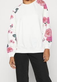 Felpa bianca con stampa floreale rosa e verde sulle maniche. Presenta una scollatura rotonda e polsini a coste. Tessuto morbido e confortevole.