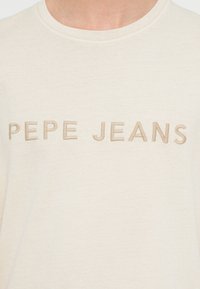 Beež puuvillane t-särk ümarselja kaelusega, millel on veidi tumedamas toonis tikitud "PEPE JEANS" logo. Pehme tekstuur ja lõõgastav istuvus.