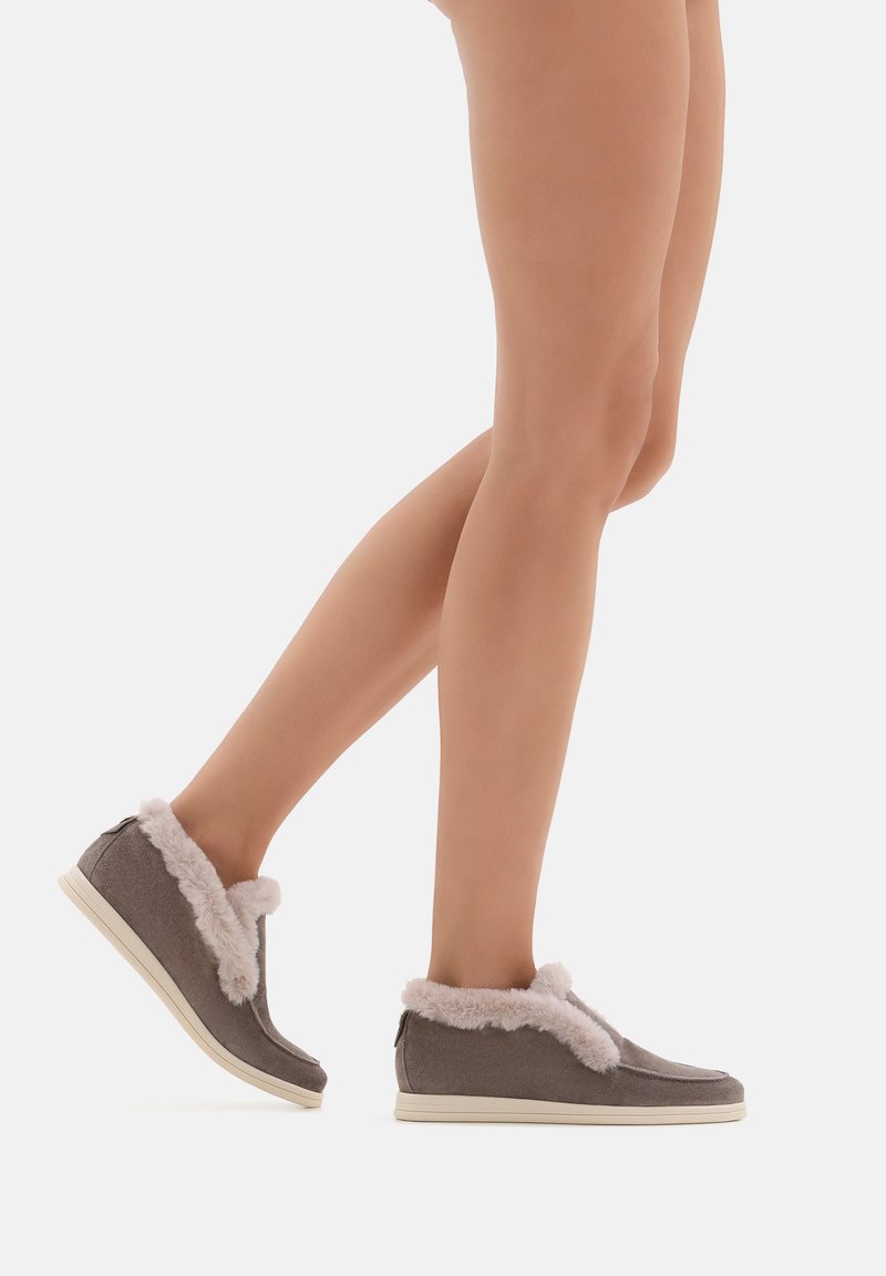 Scarpe slip-on in tessuto grigio con rifinitura in finta pelliccia rosa e suole in gomma bianche, progettate con una forma arrotondata e uno stile minimalista.