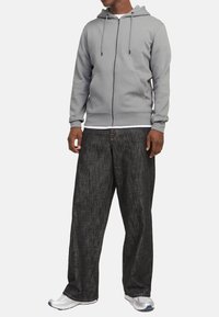 Grå zip-up hættejakke med en frontlomme, parret med løse, mørkegrå bukser med et diskret mønster. Hvid undertrøje og grå sneakers.
