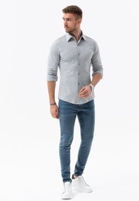 Grijze lange mouwen knoopshirt met een kraag, gecombineerd met slim-fit blauwe jeans en witte sneakers. Eenvoudig, aansluitend ontwerp met een gladde textuur.