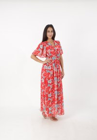 Robe maxi florale rouge avec de courtes manches évasées, décolleté en V et taille élastique, ornée de motifs floraux bleus et roses.