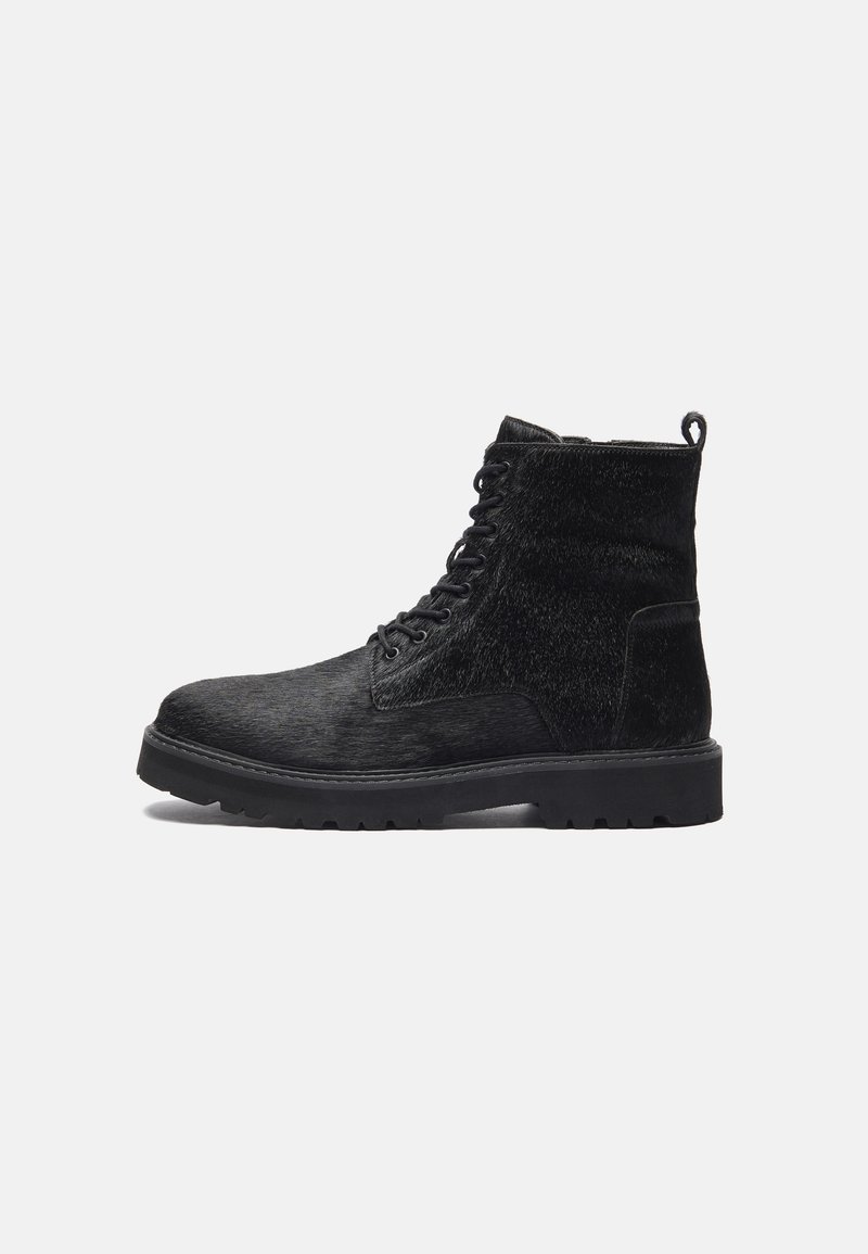 Botas pretas até ao tornozelo com um cabedal texturizado, apresentando um fecho de atacadores à frente, sola de borracha robusta e uma alça na parte de trás para facilitar o calçar.