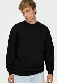 Sudadera negra con cuello redondo, puños y dobladillo acanalados. Confeccionada con un tejido suave y texturizado. Presenta un ajuste holgado y hombros caídos.