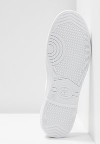 Semelle de sneaker blanche avec caoutchouc texturé, présentant des motifs circulaires et hexagonaux, des bords lisses, et un logo avec l'étiquette de taille 37.