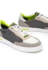 Zapatillas grises y beige con una puntera blanca perforada, acentos verdes contrastantes y una parte superior de tela texturizada. Presentan cordones blancos y una suela de goma.