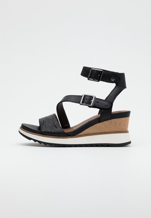 Czarna sandałowa wedge z dwiema regulowanymi paskami na kostkę, teksturowanym przednim paskiem, drewnianym obcasem oraz białą i czarną żłobioną podeszwą.