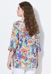 Tunic floreale in tessuto leggero, caratterizzata da un motivo vivace di fiori e foglie multicolore, con maniche a tre quarti e spacchi laterali.