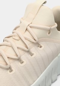 Μπεζ αθλητικό παπούτσι με υφή στην επάνω επιφάνεια, κλείσιμο με κορδόνια, επενδεδυμένο περιμετρικά κολάρο και χοντρή λευκή σόλα. Διαθέτει χαλαρά, επίπεδα κορδόνια και μεταλλικές θηλιές.