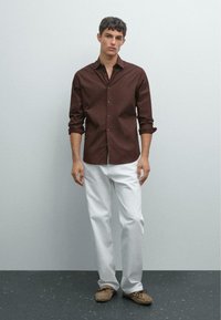 Brun skjorte med lange ærmer, i knap-op stil, parret med hvide bukser og beige mokkasiner. Glat stof og skræddersyet pasform.