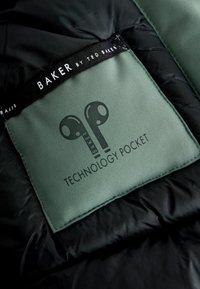 Czarna kurtka puchowa z zieloną metką. Na metce znajduje się napis "BAKER by TED BAKER" oraz wzór słuchawek z napisem "KIESZONKA NA TECHNIKĘ".